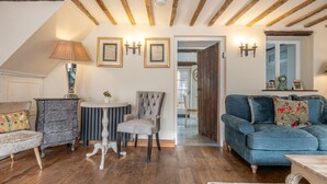 A cozy living room with a wooden ceiling, a blue sofa, a grey armchair, a white table, and a patterned armchair. - Eilmers Cottage - Beautiful 4BD in Malmesbury (Malmesbury)