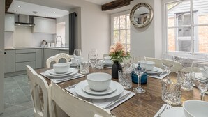 A dining area with a wooden table set for a meal, surrounded by chairs. - Eilmers Cottage - Beautiful 4BD in Malmesbury (Malmesbury)