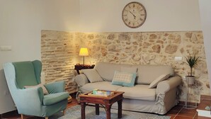 Una sala de estar con pared de piedra, un sofá, un sillón, una mesa de centro de madera y un reloj de pared.