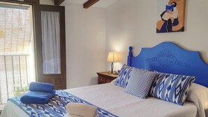 Una cama bien hecha con ropa de cama azul y blanca, un cabecero de madera y un cuadro en la pared.