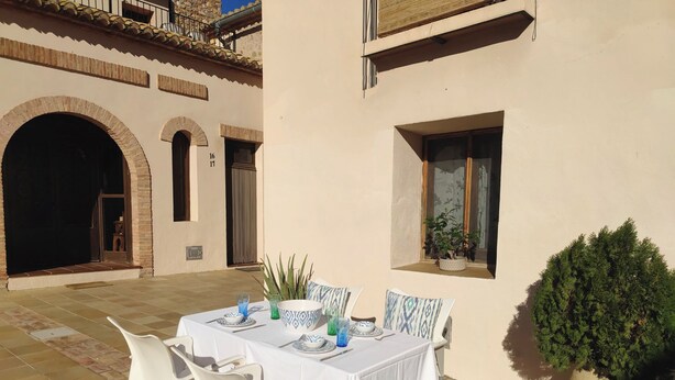 Un área de comedor al aire libre con una mesa preparada para dos, rodeada de sillas blancas.