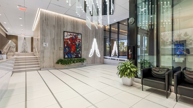Un hall d’entrée moderne avec un comptoir de réception en marbre, une grande peinture abstraite, un escalier et un espace détente agrémenté d’une plante en pot.