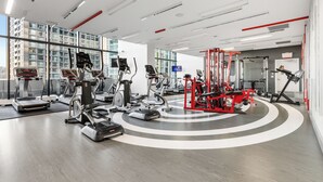 Une salle de sport moderne dotée de divers équipements pour le cardio et le renforcement musculaire, de grandes fenêtres et d’un aménagement propre et bien organisé.