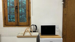 A compact kitchenette with a white refrigerator, a wooden cabinet, a window with a view of greenery, and a wooden door. - B&B "Il Melograno" cottage with private pool in Pistoia. (Pistoia)