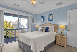 Une chambre avec un grand lit, deux lampes de chevet, une table de chevet en osier et une vue sur le balcon extérieur.