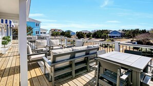 A deck with outdoor furniture, including a sofa and a table, overlooking a residential area with houses and trees. - The Sea Guld: Beach Access, Expansive Decks, Elevator & Outdoor Shower! (Wrightsville Beach)