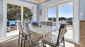Uma sala de jantar com mesa e cadeiras brancas, janelas amplas e vista para o exterior.