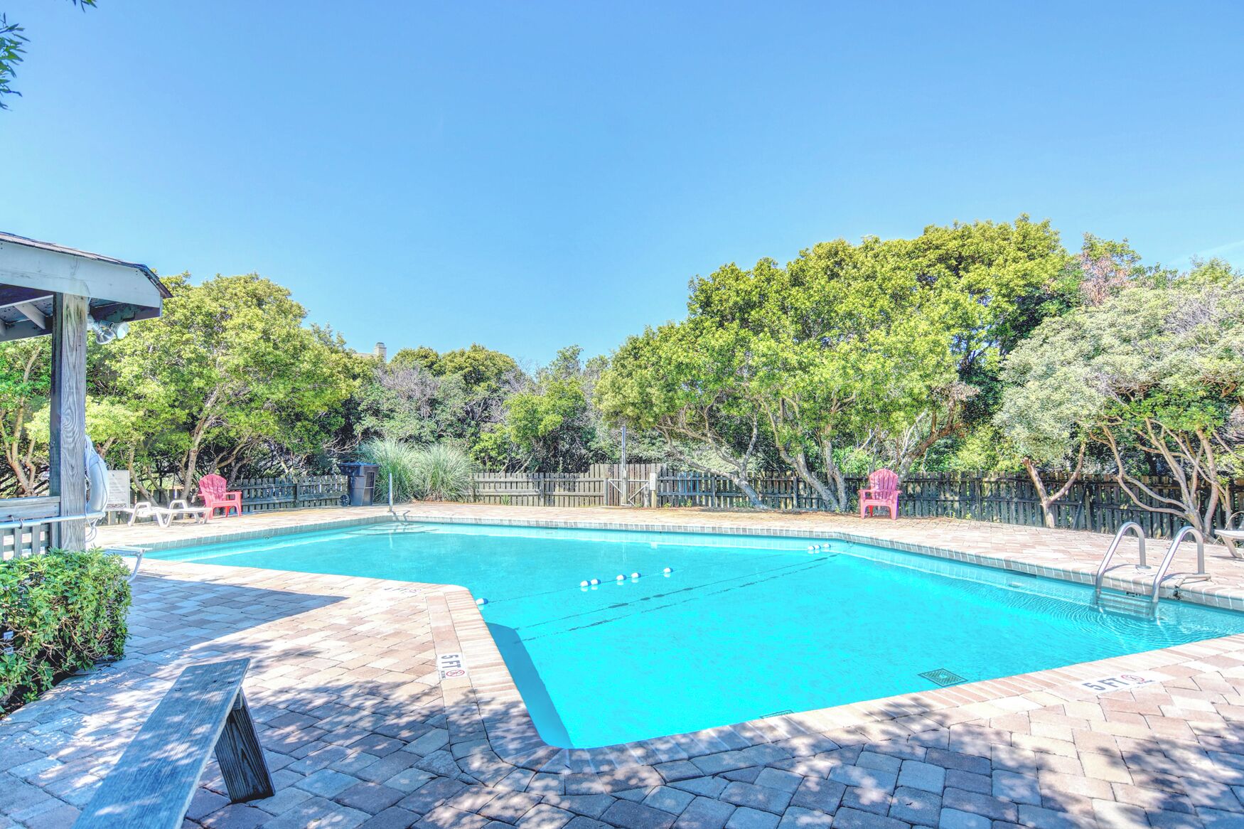 A rectangular swimming pool with clear blue water, surrounded by a brick patio.