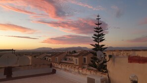 Una azotea con antenas parabólicas, un árbol y vistas a montañas lejanas bajo un cielo al atardecer.