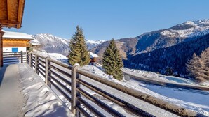Ein Holzbalkon mit Metallgeländer mit Blick auf eine verschneite Berglandschaft.