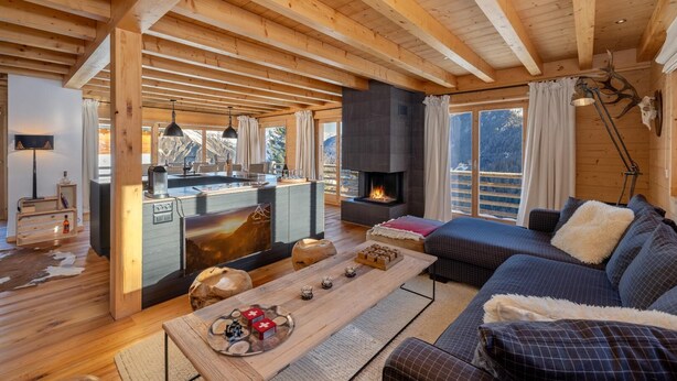 Ein gemütliches Blockhaus-Interieur mit Kamin, Essbereich und einer Sitzecke mit Sofa und Couchtisch.