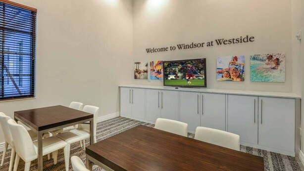 A conference room with a wooden table and white chairs, a television on the wall, and artwork depicting sports and leisure activities.