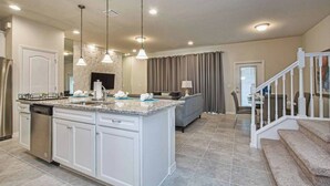 A spacious kitchen with a central island, white cabinetry, and a dishwasher. There is a dining area with a table and chairs, and a staircase leading to another level. - Spacious Townhome, Gated Resort, 5BD, Pool (8922) (Kissimmee)