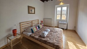 Une chambre à coucher avec un lit en bois, une fenêtre, un radiateur et une petite table avec une lampe.
