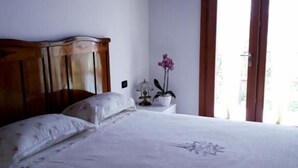 Een slaapkamer met een bed, een nachtkastje, een potplant en een raam met gordijnen.