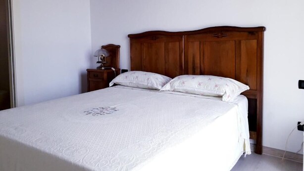 Een slaapkamer met een houten hoofdbord, twee kussens, een nachtkastje en een nachttafel.