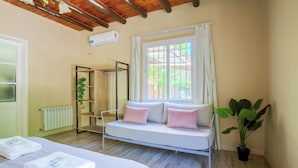 A bedroom with a bed, a sofa, a window with curtains, a radiator, and a potted plant. - MOT Besares (Chacras de Coria)