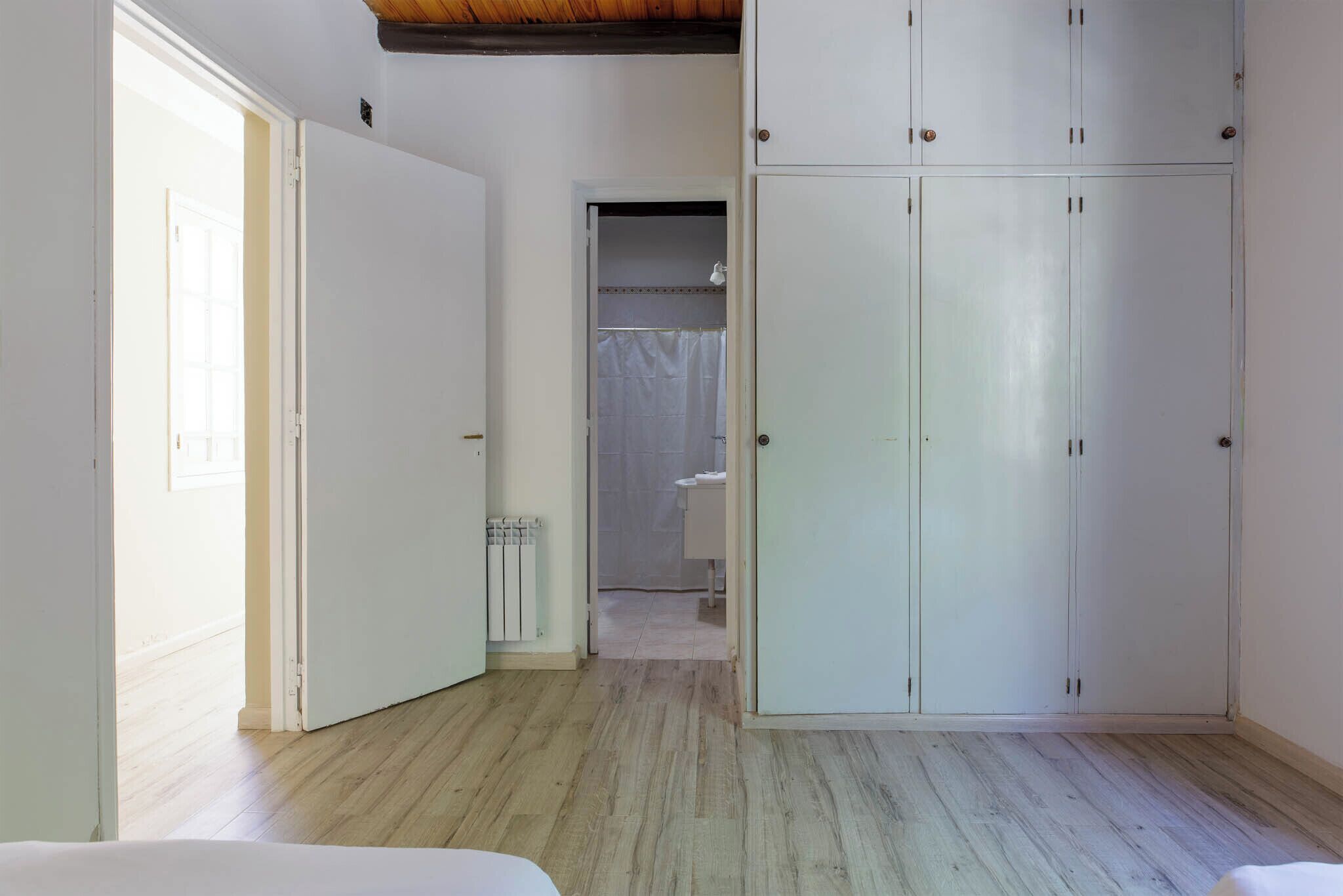 Una habitación con suelo de madera, paredes blancas y un amplio armario con múltiples puertas.