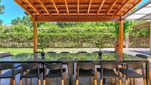 An outdoor patio with a glass-top table and chairs, surrounded by a wooden pergola and a view of a garden. - MOT Besares (Chacras de Coria)