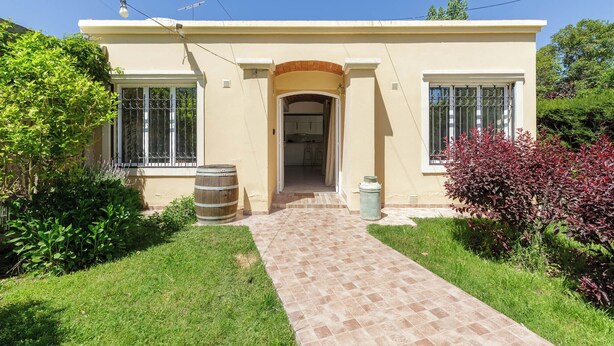 A two-story house with a tiled entrance walkway, a garage door, and a small porch area. - MOT Besares (Chacras de Coria)