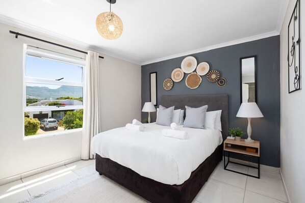 Enjoy a restful stay in this cozy room with a large bed, a bedside table, and a lamp, offering a view of the surrounding landscape.