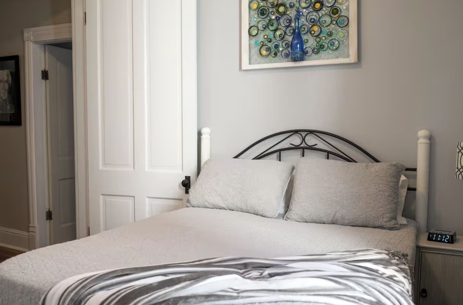 A bedroom with a bed, a nightstand, a wall clock, and a door.