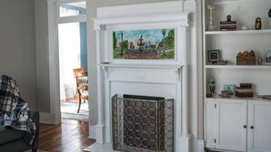Un salón con chimenea blanca, un cuadro encima y una estantería a la derecha.