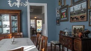 Un comedor con una mesa preparada para cuatro, sillas de madera, una araña y una pared decorada con cuadros enmarcados.