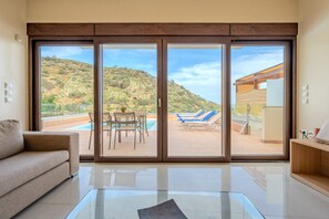 Una sala de estar moderna con un amplio ventanal corredero que da a una zona de piscina con sillas de descanso y una mesa.