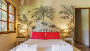 A double bed with red pillows, two bedside tables with lamps, and a mural of palm trees on the wall. - MOT Alzaga (Chacras de Coria)
