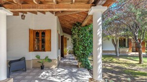 A covered walkway with a tiled floor, wooden beams, and a potted plant. - MOT Alzaga (Chacras de Coria)