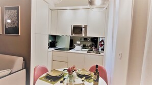 Une cuisine compacte dotée d’appareils électroménagers modernes, un coin repas avec des chaises roses et un canapé.