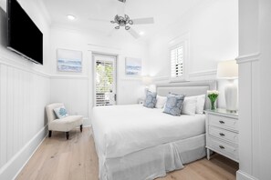 A bedroom with a large bed, a chair, a nightstand, a TV, and a ceiling fan.