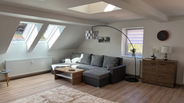 Een moderne woonkamer met een grijze bank, een houten bijzettafeltje, een zacht vloerkleed, een staande lamp en een kast.