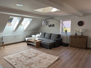 A modern living room with a grey sofa, a wooden coffee table, a fluffy rug, a floor lamp, and a cabinet. - Apartments Badallee 4, Bad Schandau, Apartment No. 7, Loft 75m2 (Bad Schandau)