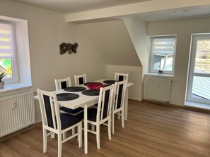 A dining area with a white table and chairs, a potted plant, and a decorative wall piece. - Apartments Badallee 4, Bad Schandau, Apartment No. 7, Loft 75m2 (Bad Schandau)