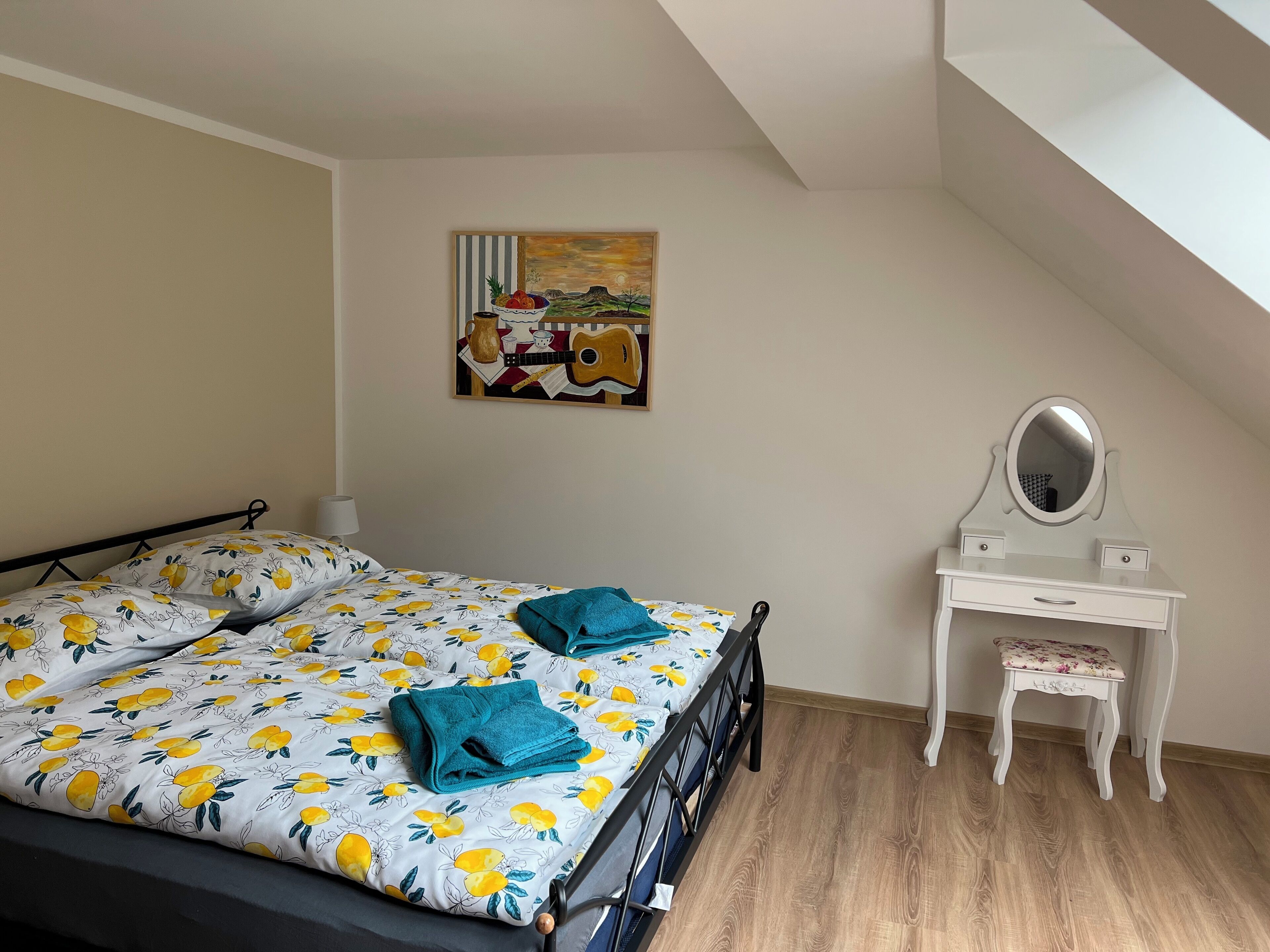 A bedroom with a bed, a small white dresser with a mirror, and a painting on the wall.