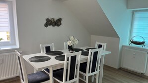 Een eethoek met een witte tafel en stoelen, een vaas met bloemen en decoratieve wandkunst.