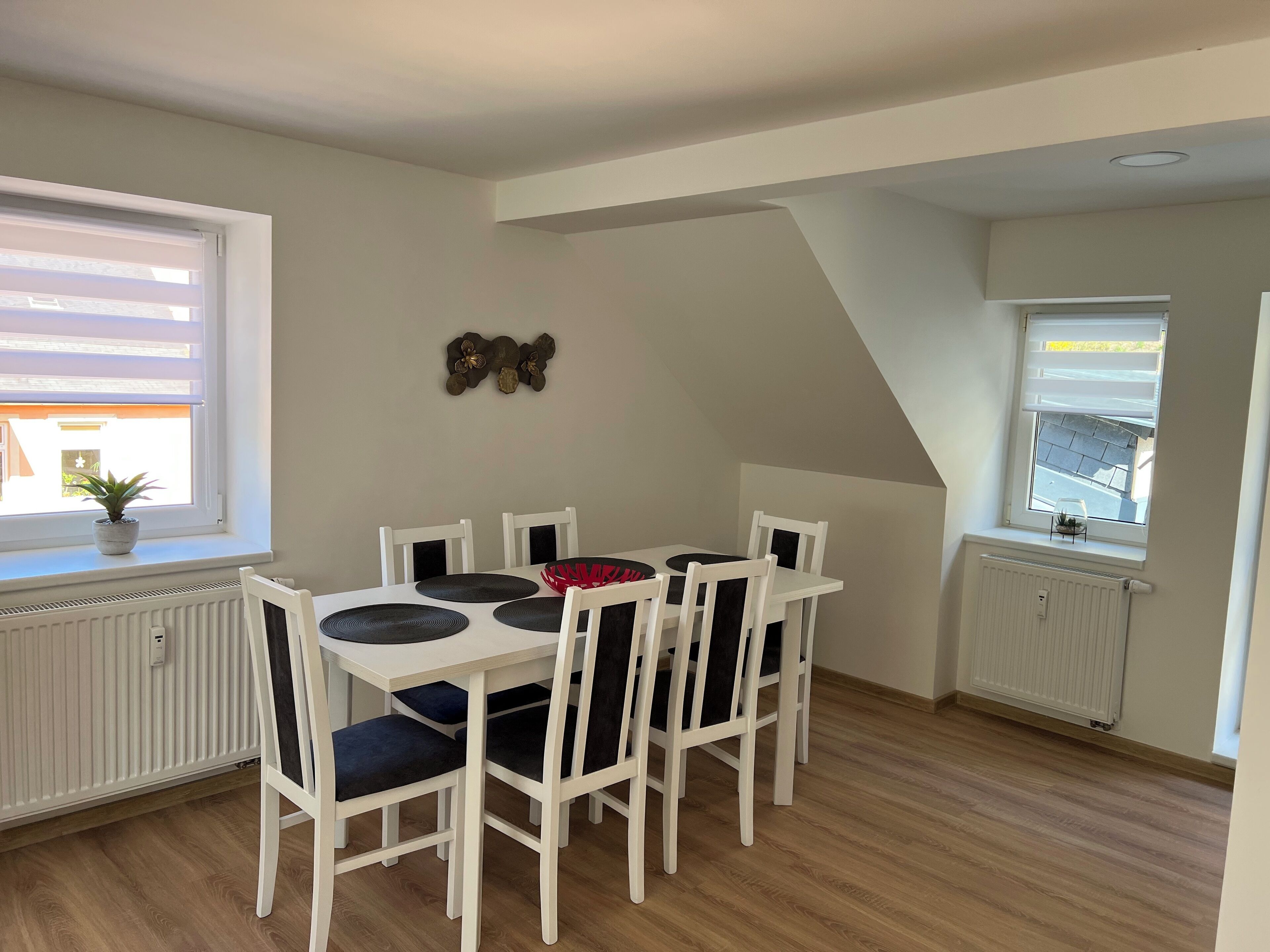 Spiseområde med et hvidt bord, sorte og hvide stole og en potteplante på vindueskarmen.
