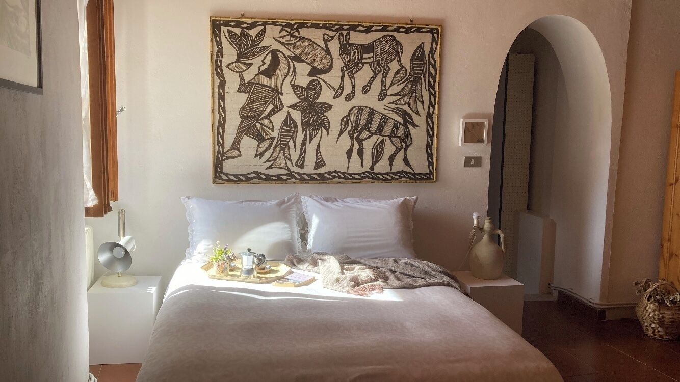 Une chambre à coucher avec un grand lit, une table de chevet avec une lampe, une œuvre d’art accrochée au mur et une arche en bois.