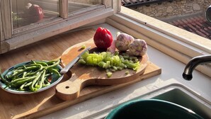 A kitchen with a wooden cutting board, a red bell pepper, and a bowl of green beans. A window with a view of mountains is visible. - Charming house surrounded by nature, 15 minutes from the sea and the French Riviera. (Liguria)