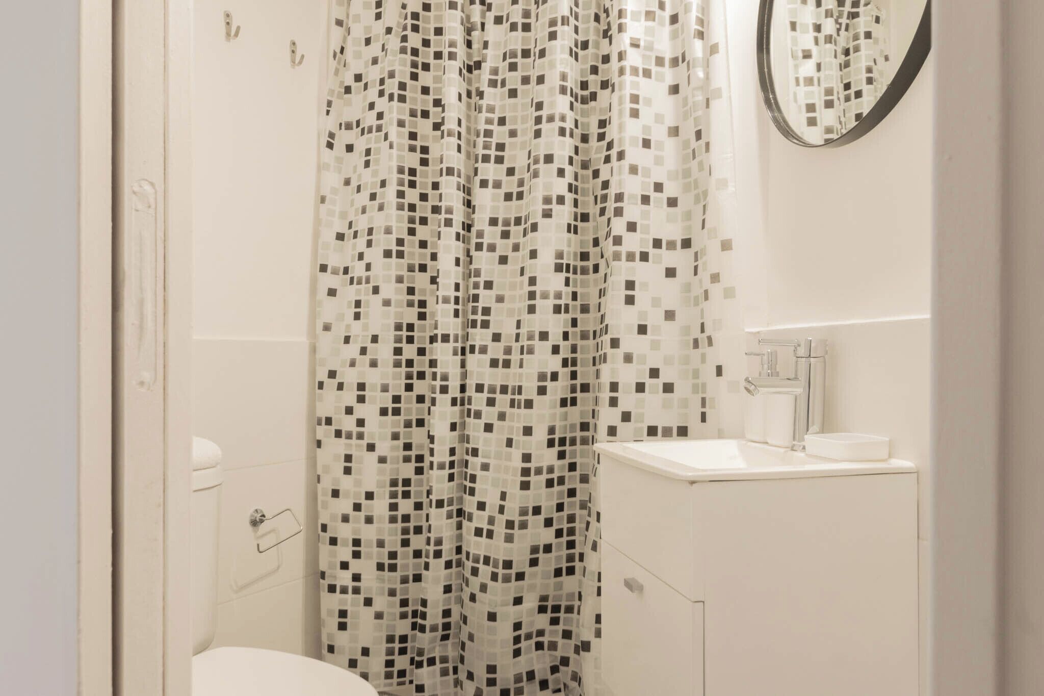 Un baño con cortina de ducha de azulejos, un inodoro y un lavamanos con espejo.
