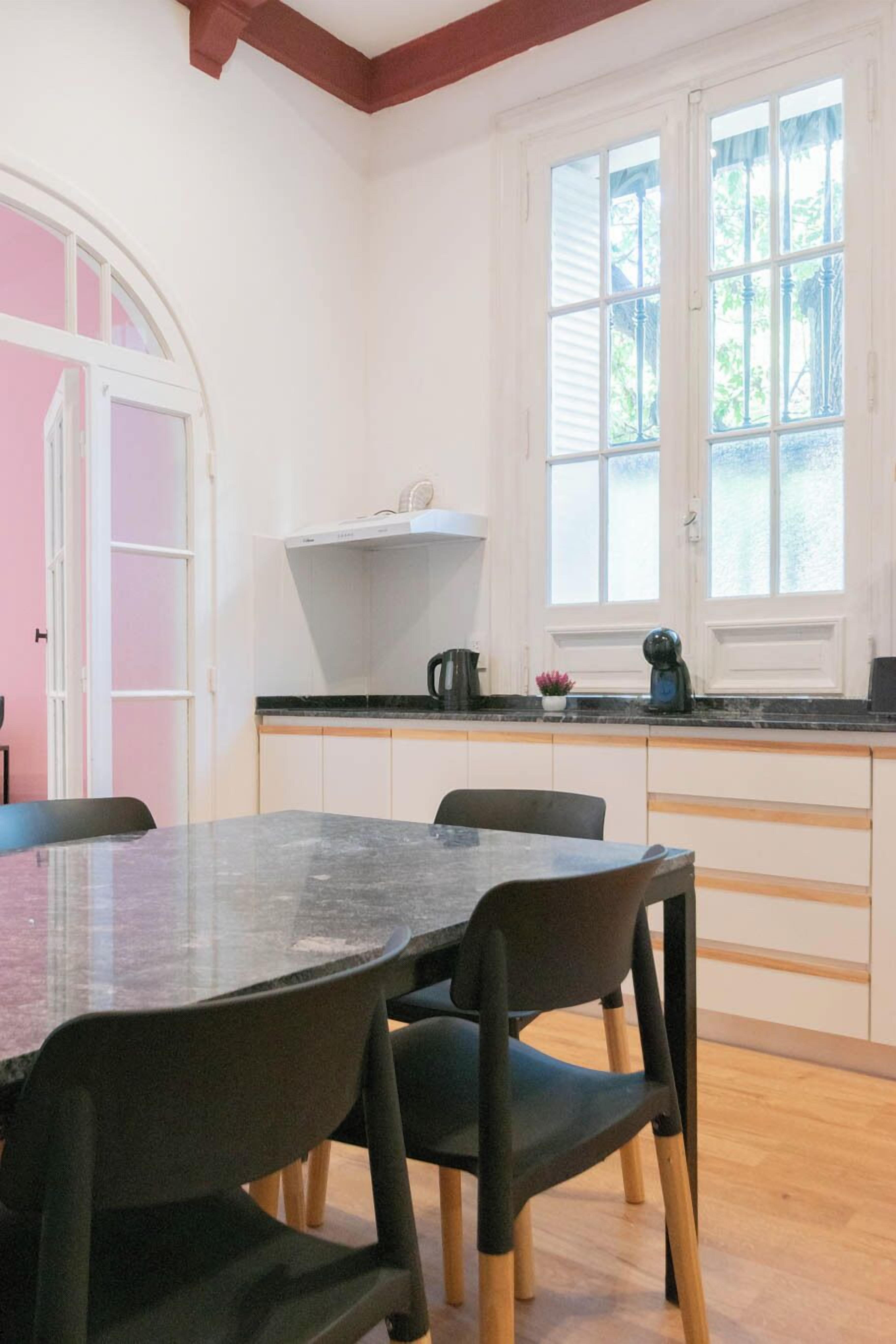 Una cocina con encimera de mármol, armarios blancos y una ventana con vistas a la vegetación.