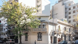 A street view with a building featuring a balcony, a tree, and parked cars. - MOT Mansion Paz (Buenos Aires)