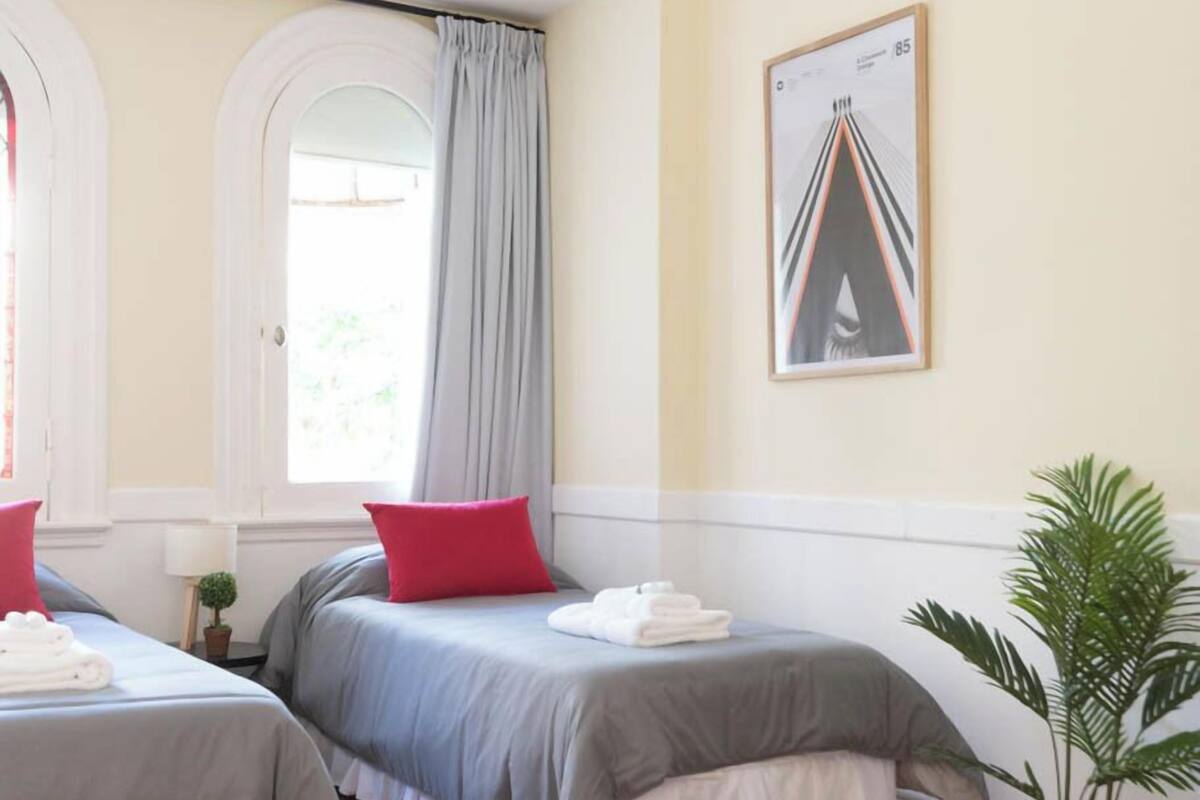 Une chambre d’hôtel avec deux lits, une plante en pot et une fenêtre avec des rideaux.
