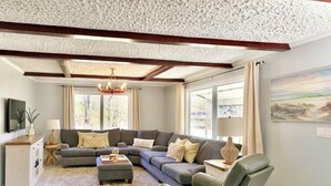 Una sala de estar con un sofá modular, una mesa de centro y un sillón. Hay un televisor a la izquierda y un cuadro en la pared.