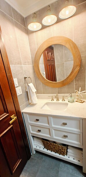 Une salle de bain avec un meuble-lavabo en bois, un miroir rond et trois appliques murales.