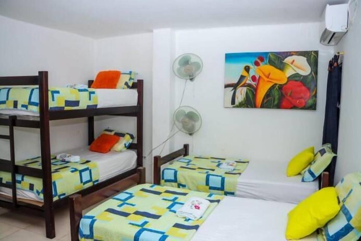 A dormitory room with bunk beds, a wall-mounted fan, and a painting.
