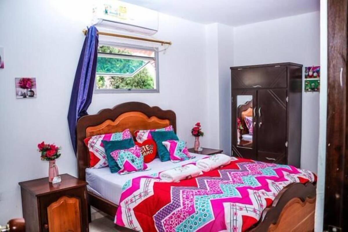 A bedroom with a wooden bed, colorful bedding, a small bedside table with a vase, and a wardrobe.