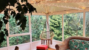 Amplia habitación con ventanas grandes, sofá de mimbre, una mesa de centro de vidrio y una silla colgante.